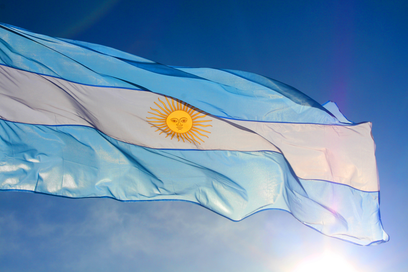 Argentina flag waving against sun and blue sky. Photo 58061610 © Veronika Peskova - Dreamstime.com